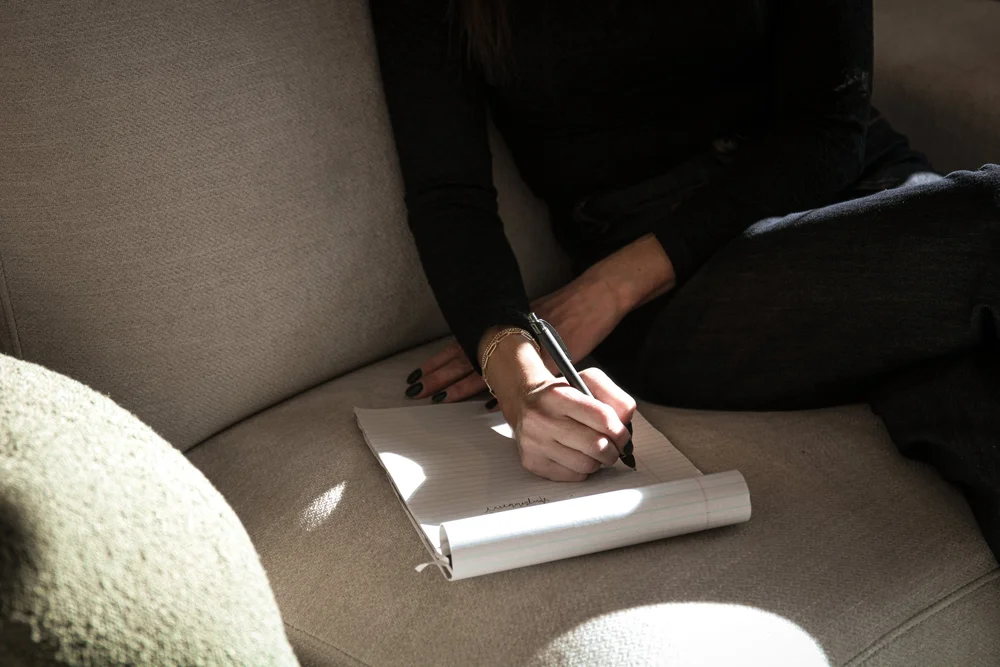 a woman sits on a couch and takes notes in her notepad
