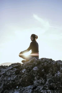 A person sits in a meditative pose on a hilltop